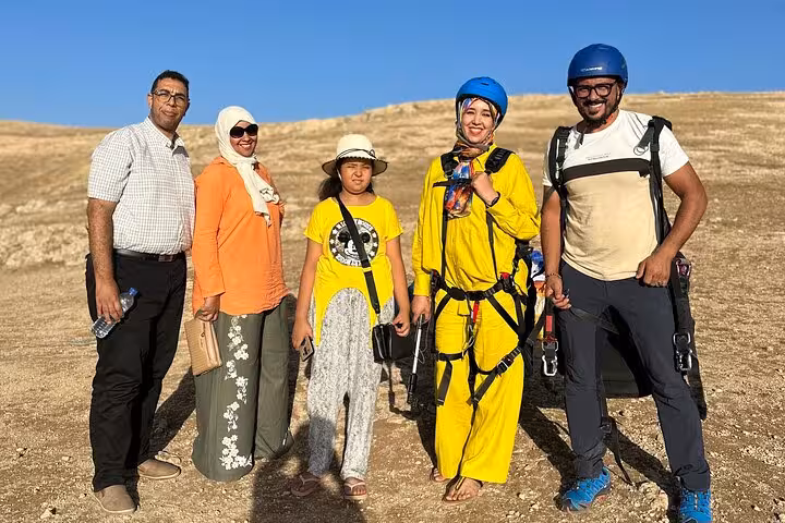 Happy group in colorful outfits ready for paragliding adventure in Agafay Desert near Marrakech under clear blue sky.