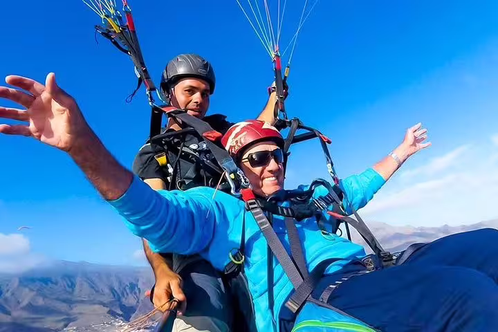Excited paragliding duo enjoying the clear skies and panoramic mountain views at 1000 meters above the ground.