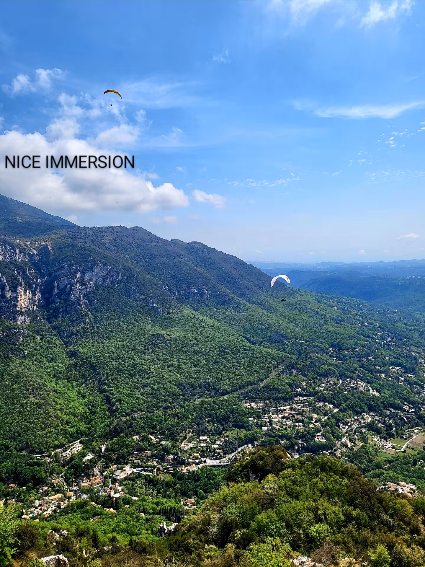 Scenic view of paragliders soaring over the lush, mountainous landscape of the French Riviera under a vibrant blue sky.