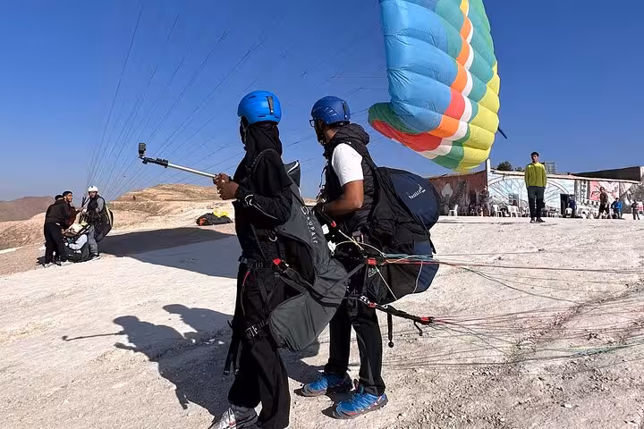 Paragliders prepare for takeoff in the Agafay Desert near Marrakech, showcasing vibrant parachutes and clear blue skies.