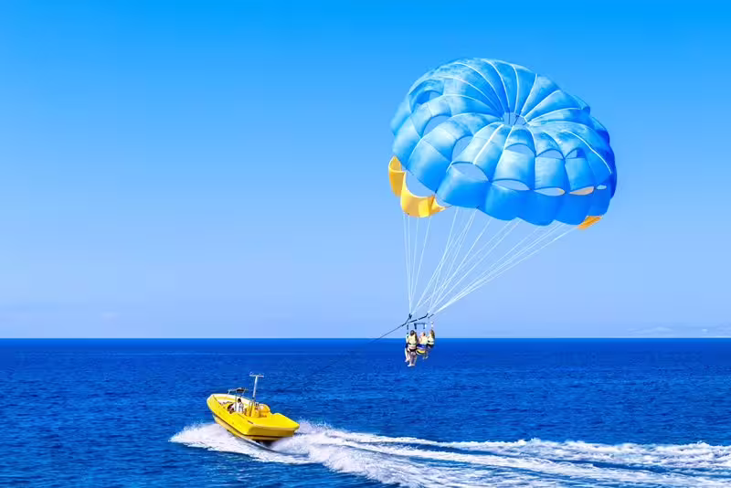 Parasailing over the Red Sea in Sharm El Sheikh, speedboat towing blue canopy on water sports day trip