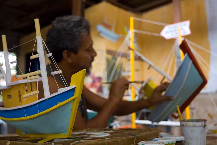 Artisan painting colorful model boats in Paraty, showcasing local craftsmanship on a cultural tour.