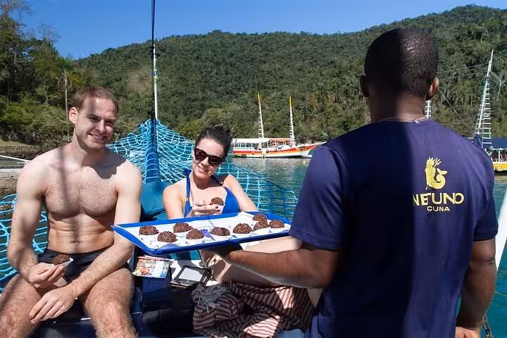 Tourists enjoying desserts on a boat with lush green hills in the background, highlighting Paraty boat tour delights.