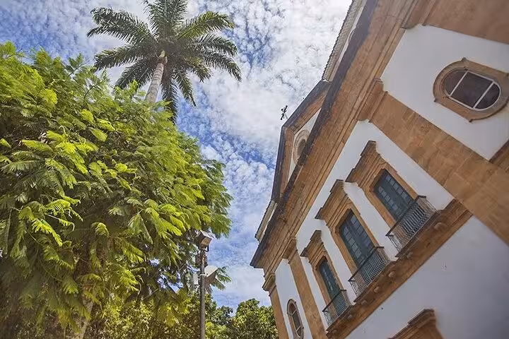 Upward view of historic colonial architecture and palm trees against a blue sky in Paraty's historical center.