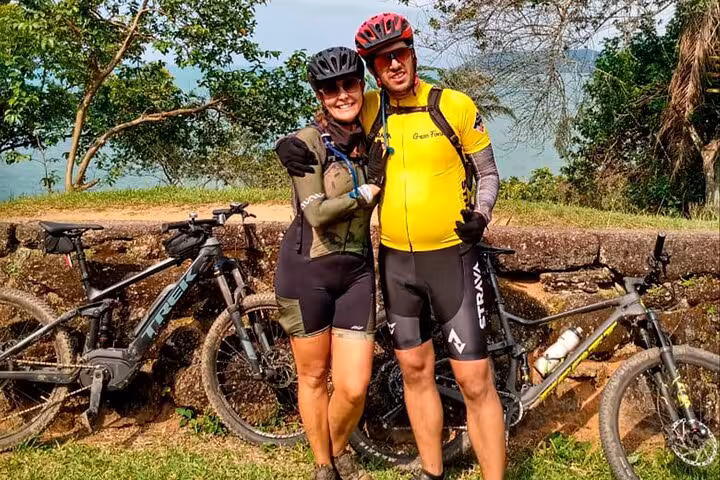 Couple in cycling gear enjoying a scenic view during a 2-hour guided bike tour in Paraty, surrounded by lush greenery.