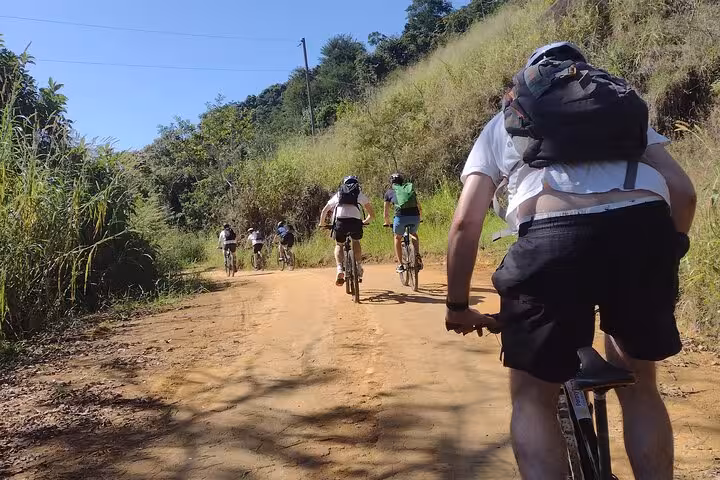 Riders navigating a dirt path surrounded by greenery on a guided bike tour in Paraty's picturesque landscape.