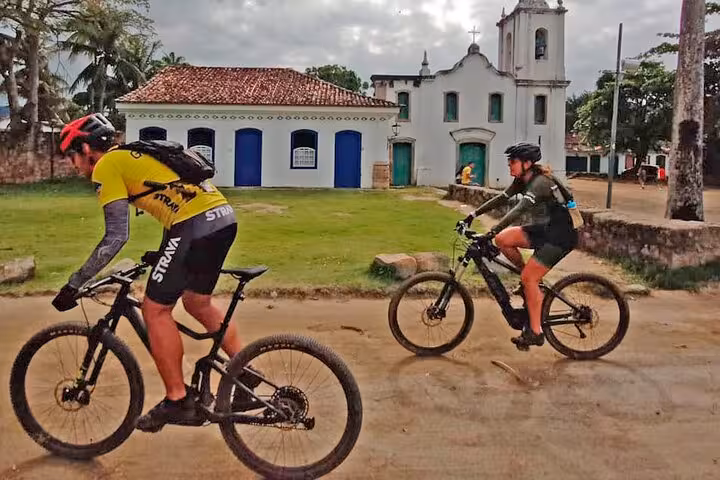 Cyclists passing historical architecture during a guided bike tour in Paraty, showcasing the town's cultural charm.