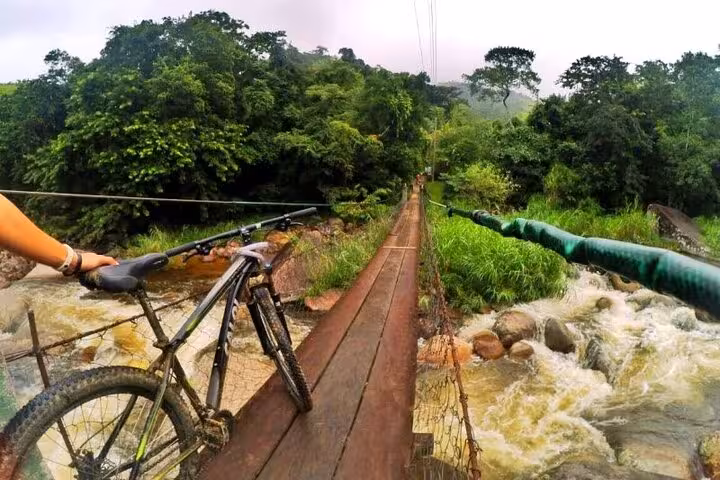 Biker crossing a narrow wooden bridge over a rushing river in Paraty, highlighting the adventurous 2-hour guided bike tour.
