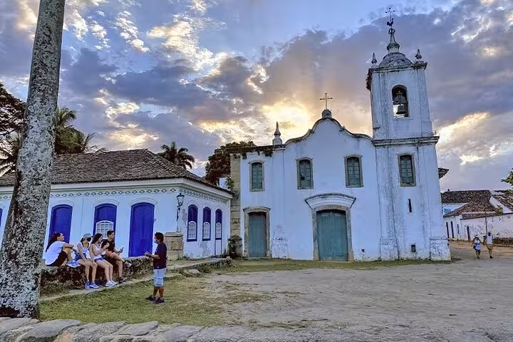 Sunset view of a historic church in Paraty, Brazil, with tourists enjoying the serene atmosphere on a historical tour.