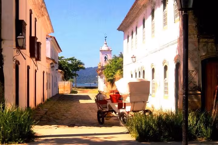 Charming street in Paraty's historical center featuring a horse-drawn carriage and colonial church with ocean view.