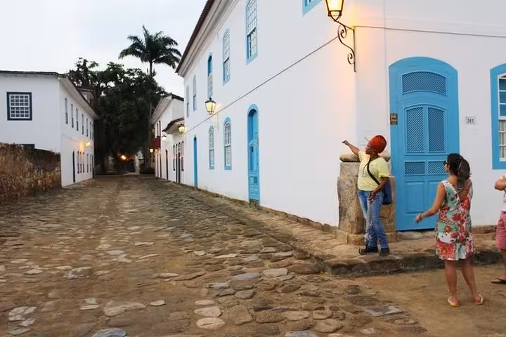 Tour guide points to historical architecture in Paraty's cobblestone street, showcasing colonial blue and white houses.