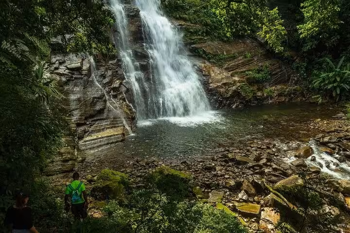 Adventurers gazing at the majestic Melancia Waterfall amidst vibrant jungle foliage in Paraty.