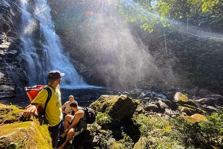 Visitors enjoying misty spray at the base of Paraty's Melancia Waterfall during an adventurous trekking tour.