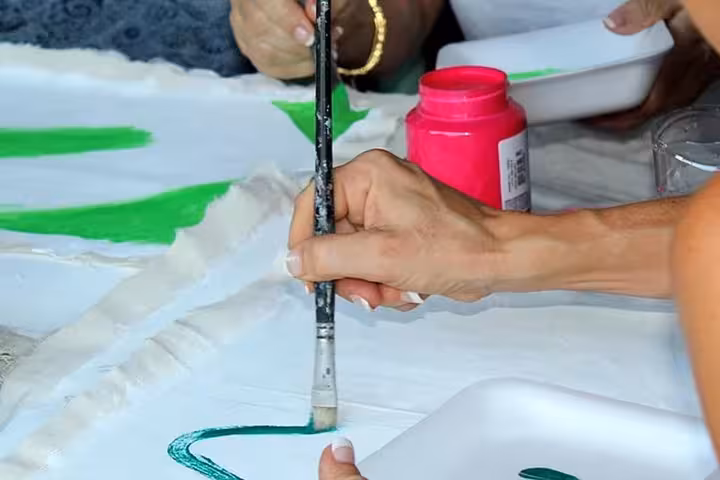 Participants in Paraty painting class use vibrant green paint to create art, highlighting creativity and learning.