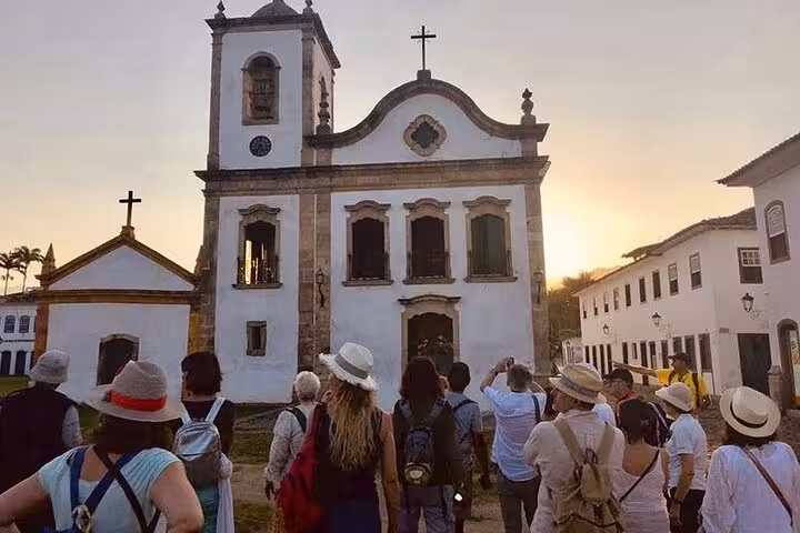 Tourists explore a historic church in Paraty's center during a private walking tour by Paraty Tours at sunset.