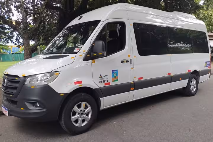 Comfortable white minivan used for shared transfers from Paraty to Rio de Janeiro, parked under lush green trees.
