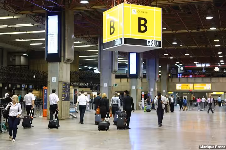 Interior view of GRU Airport's check-in area with travelers, highlighting the shared shuttle service to São Paulo.