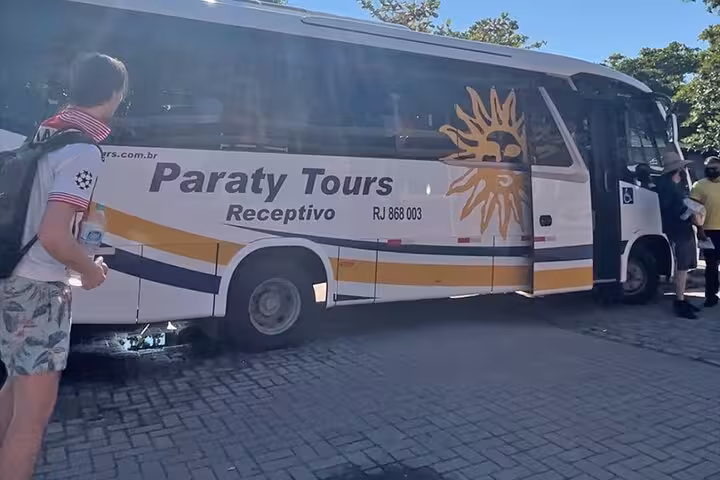 Tourist approaching a Paraty Tours bus for a shared transfer service to Rio de Janeiro, emphasizing group travel convenience.