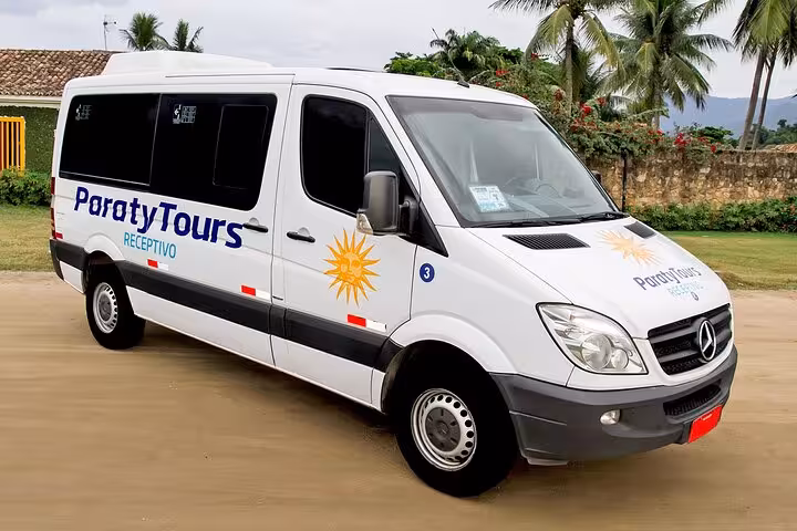 Paraty Tours minivan ready for shared transfer service from Paraty to Rio de Janeiro hotels, parked amidst lush greenery.