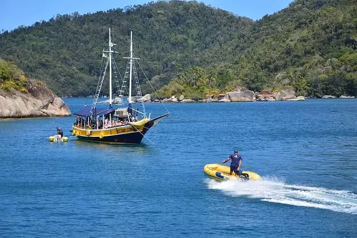 A scenic view of a Paraty Tours boat tour with a motorboat navigating crystal-clear waters against lush green hills.