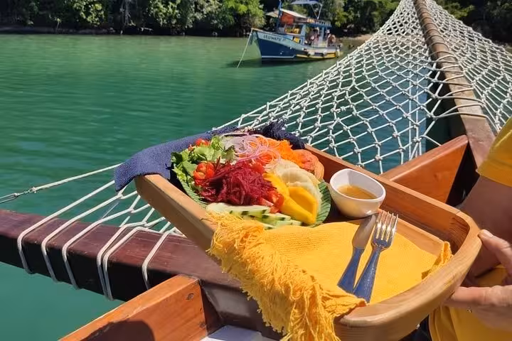 Colorful fresh salad on a boat deck during a Paraty Tours boat tour, with lush greenery and turquoise waters in view.