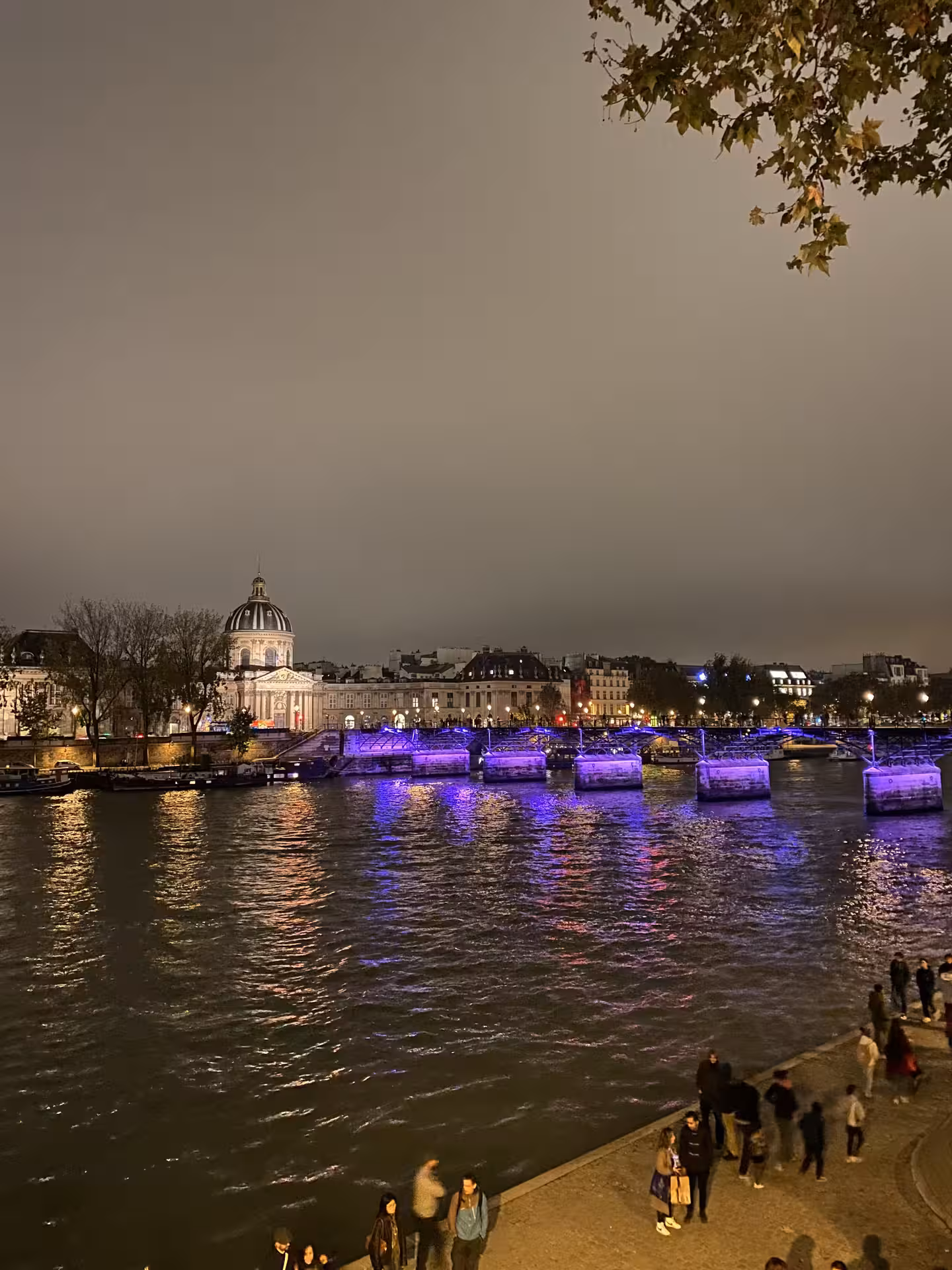Illuminated Paris riverbank with colorful lights reflecting on the Seine, highlighting a scenic crime tour route.