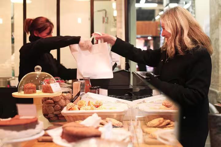A customer receiving a pastry bag from a vendor in a Parisian bakery on a private food tour.