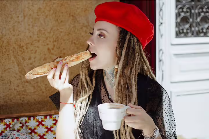 Woman in a red beret enjoying a baguette and coffee, capturing the essence of a Paris Le Marais food tour experience.
