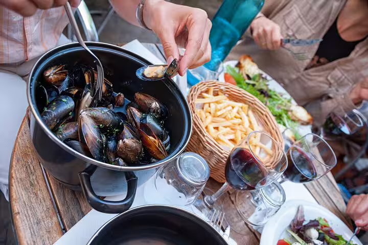 People enjoying mussels, fries, and wine at an outdoor café table in Paris' Le Marais during a French walking food tour.
