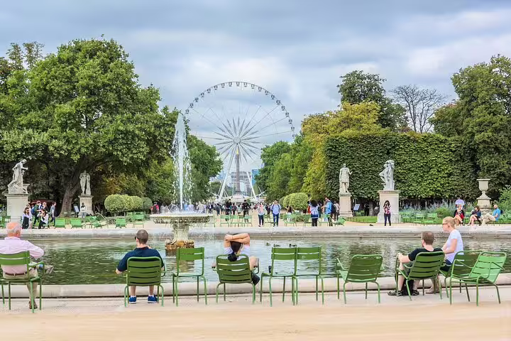 Visitors relax by a fountain in a lush Paris park with a Ferris wheel in the background, part of a Montmartre and Eiffel Tower tour.