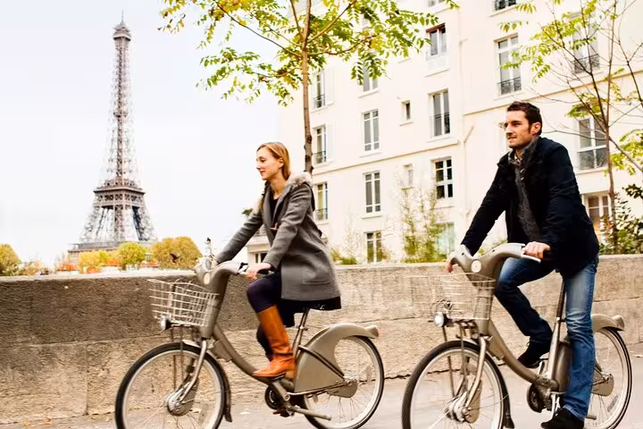 Two riders cycling near the Eiffel Tower on a Paris Seine bicycle tour, with optional Louvre Museum entrance