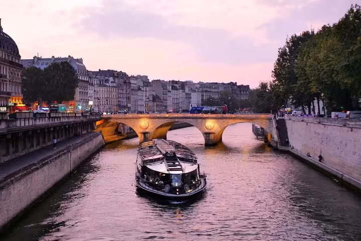 Seine River cruise at sunset in Paris under a stone bridge, included with Full Day Paris City Pass hop-on hop-off