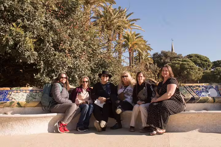 Group of tourists enjoying the iconic mosaic benches in Park Güell on a sunny day.