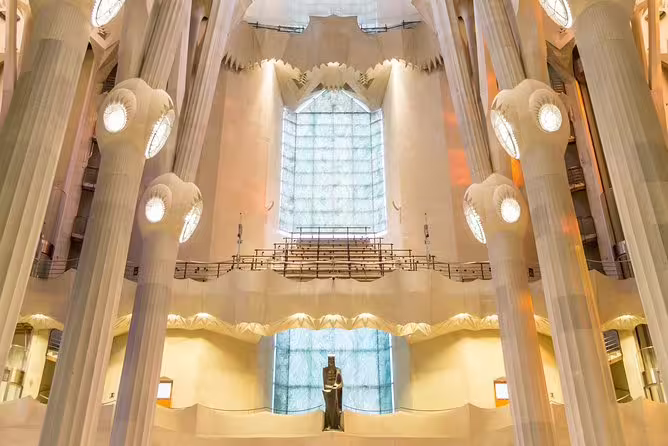 Majestic interior of Park Guell with towering columns and a large stained glass window, highlighting Gaudí's design.