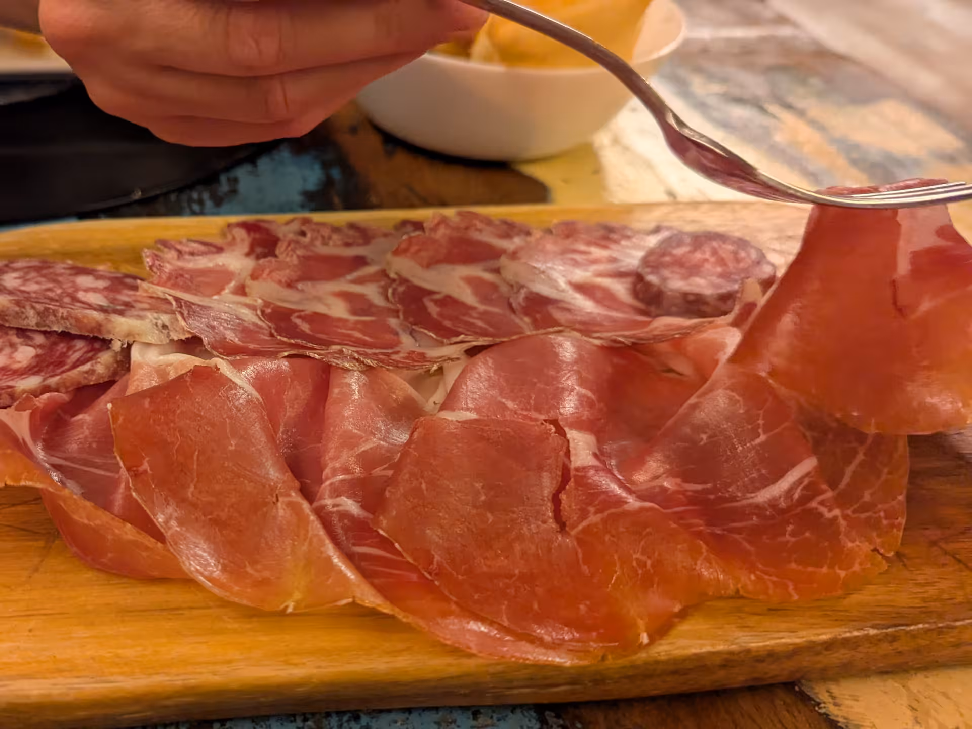 Close-up of Parma ham slices being lifted, showcasing the quality and texture of this Italian delicacy.