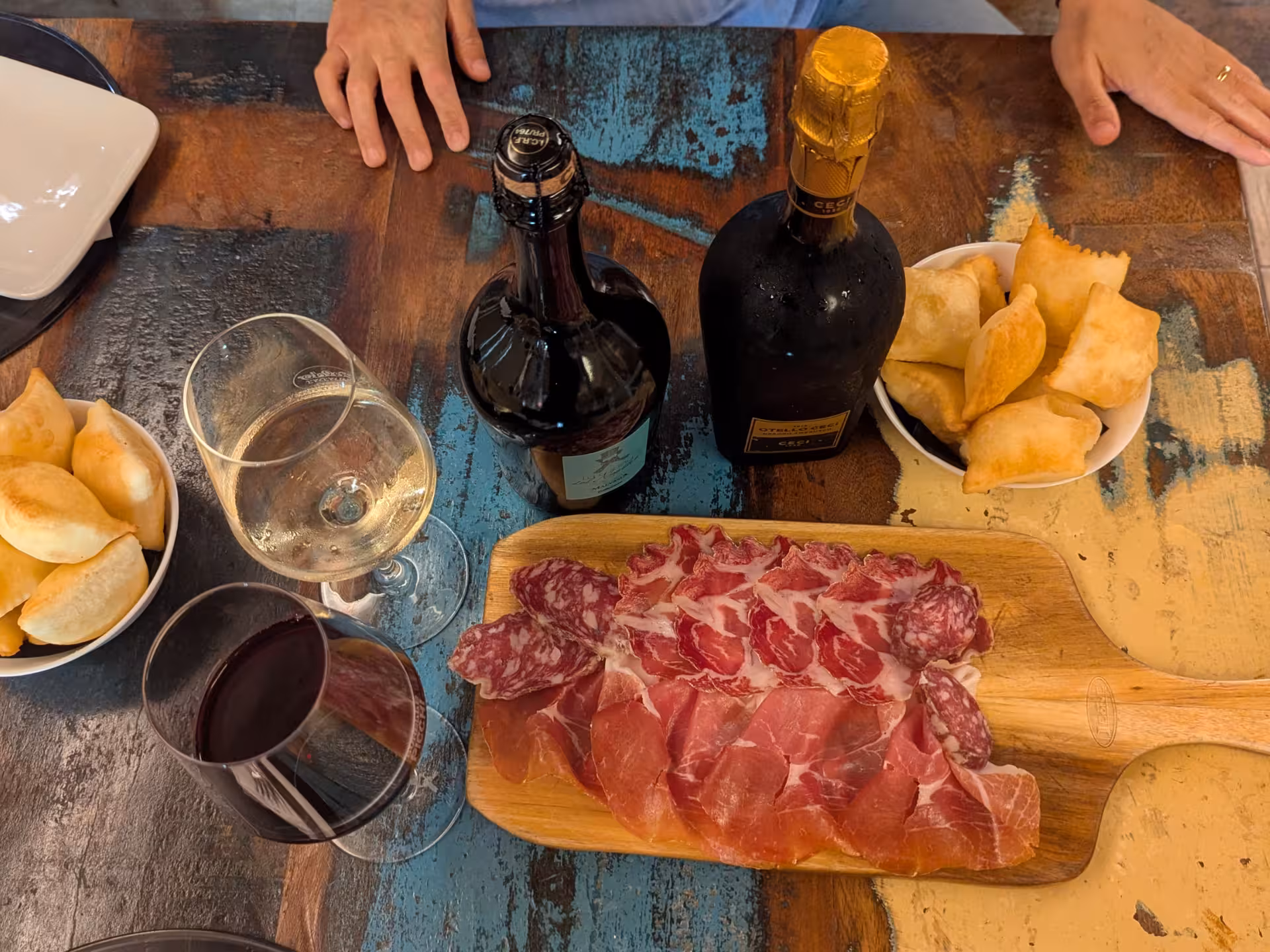 A wooden board with Parma ham, salami, and wine glasses, complemented by fried dough, perfect for tasting in Parma.