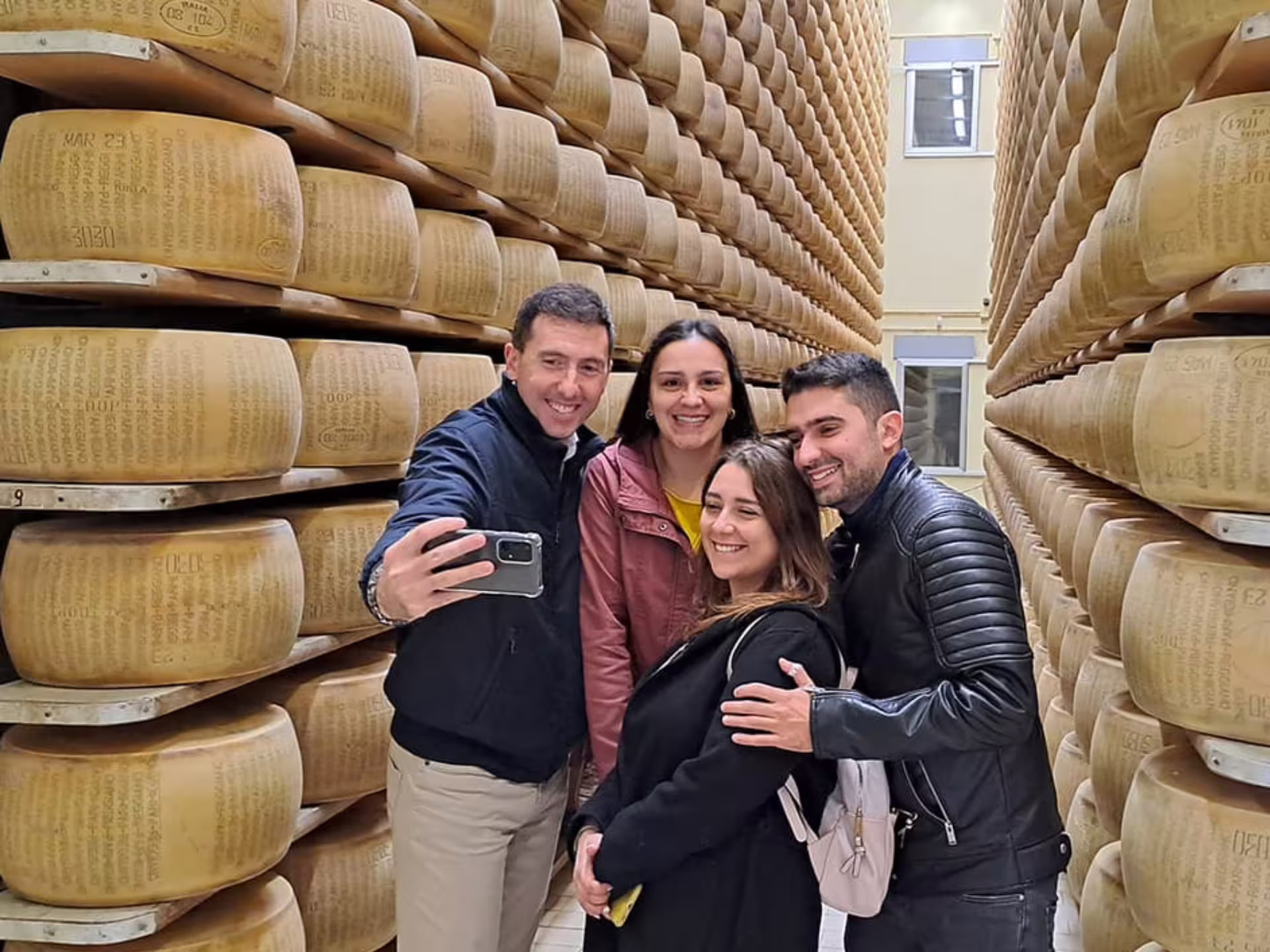 Visitors take a selfie surrounded by aging Parmesan cheese wheels on a factory tour near Parma.