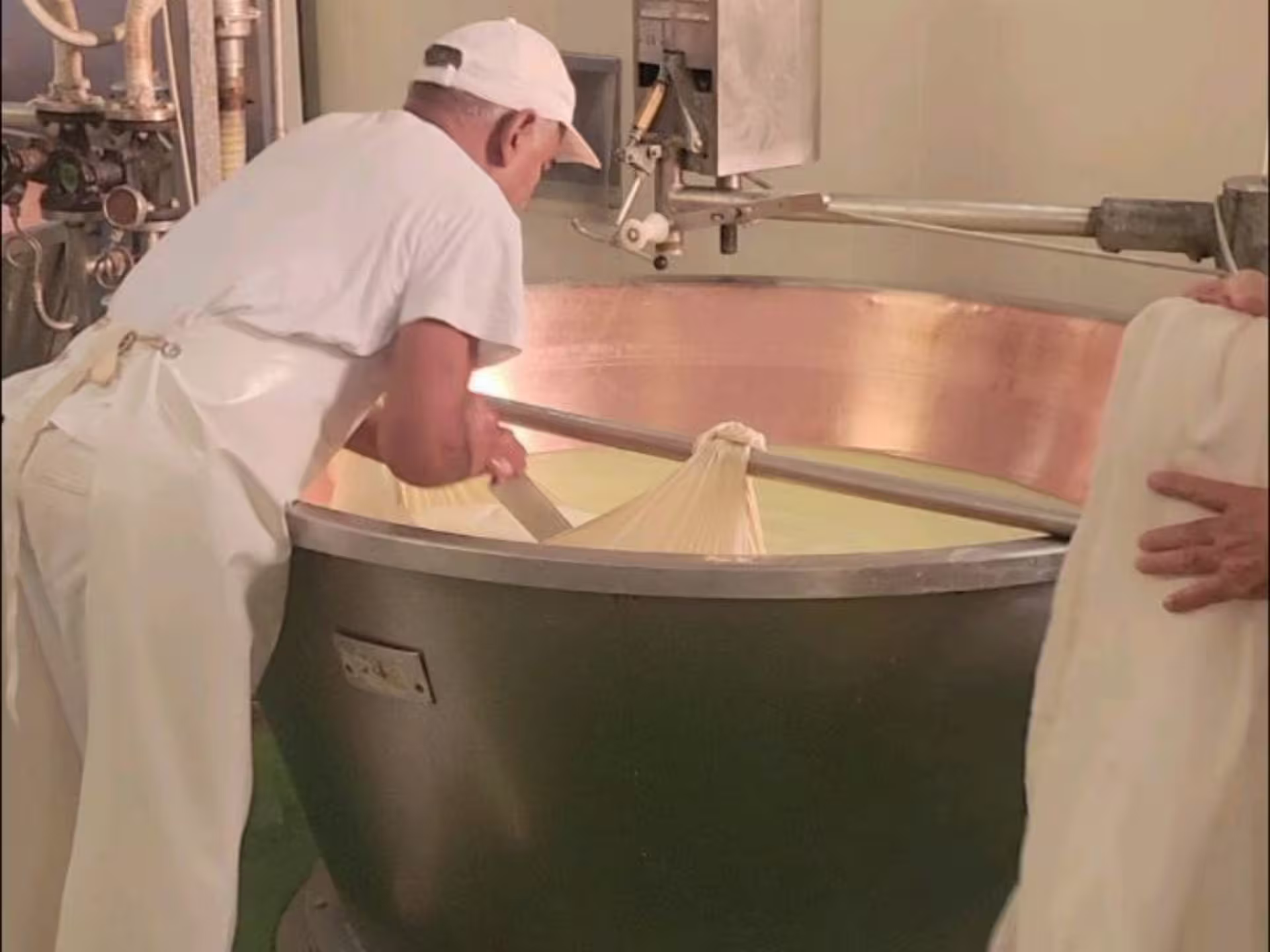 Cheesemaker stirring curds in copper vat during Parmigiano Reggiano tour and tasting near Modena