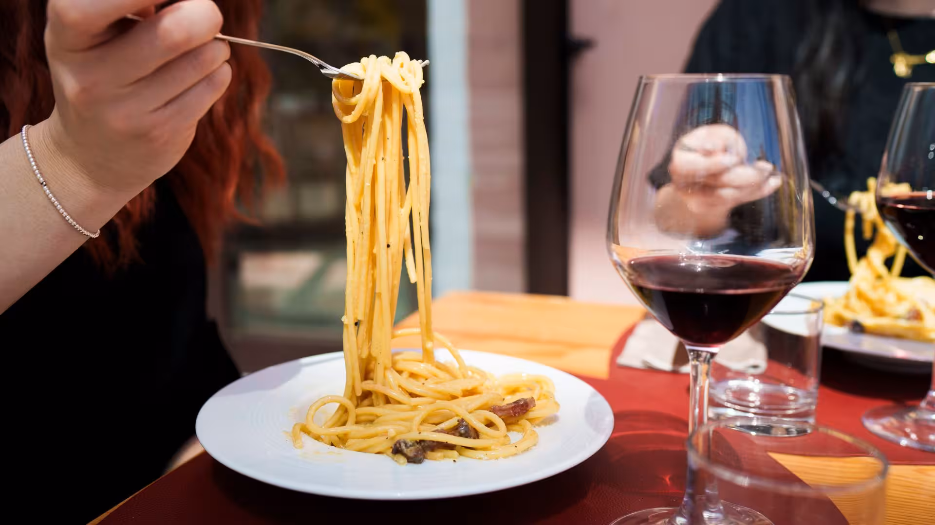Close-up of pasta carbonara twirled on a fork with red wine, highlighting a hands-on cooking class in Olbia.