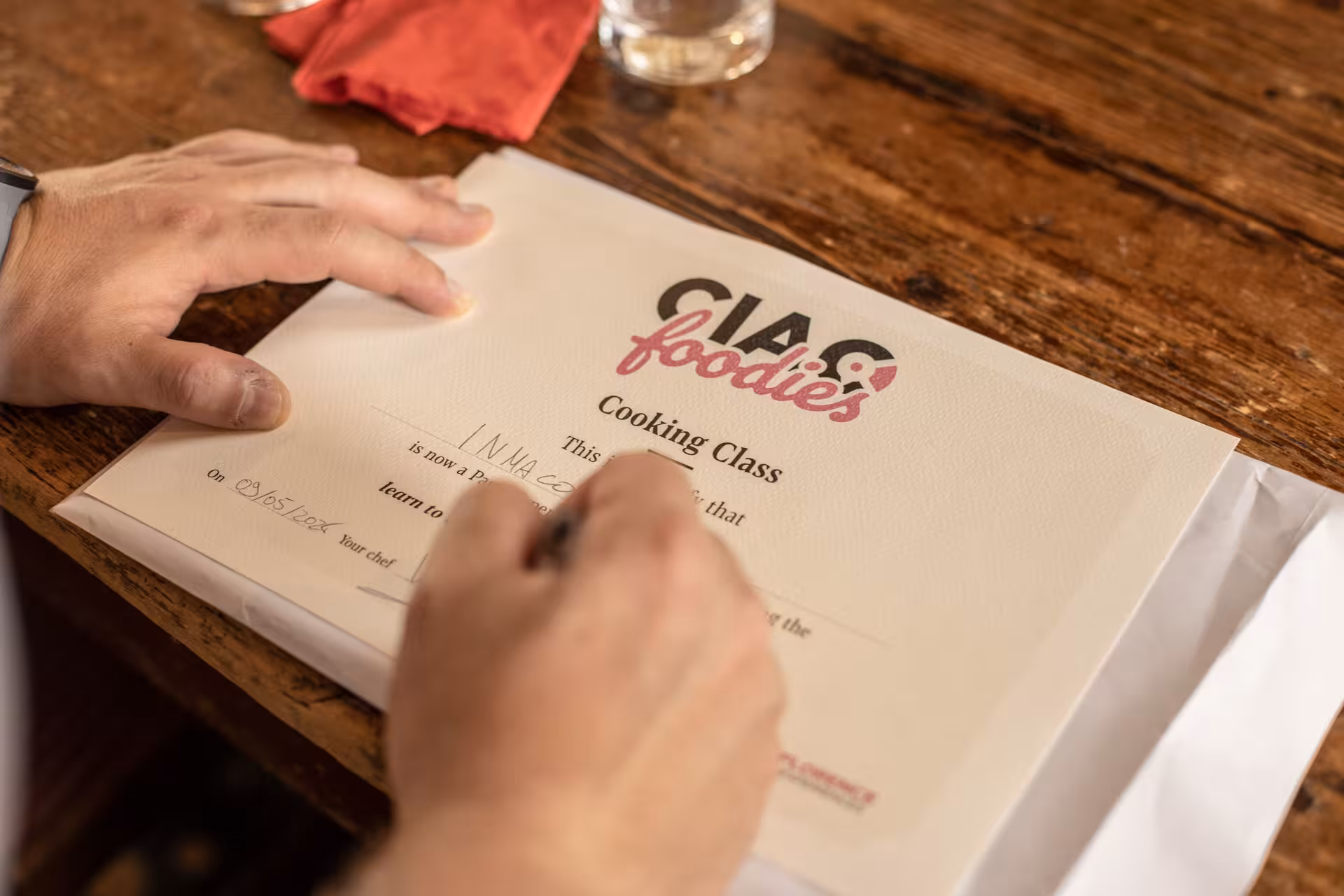 Close-up of hands writing on a cooking class certificate at Pasta Lovers Cooking Class in Florence.