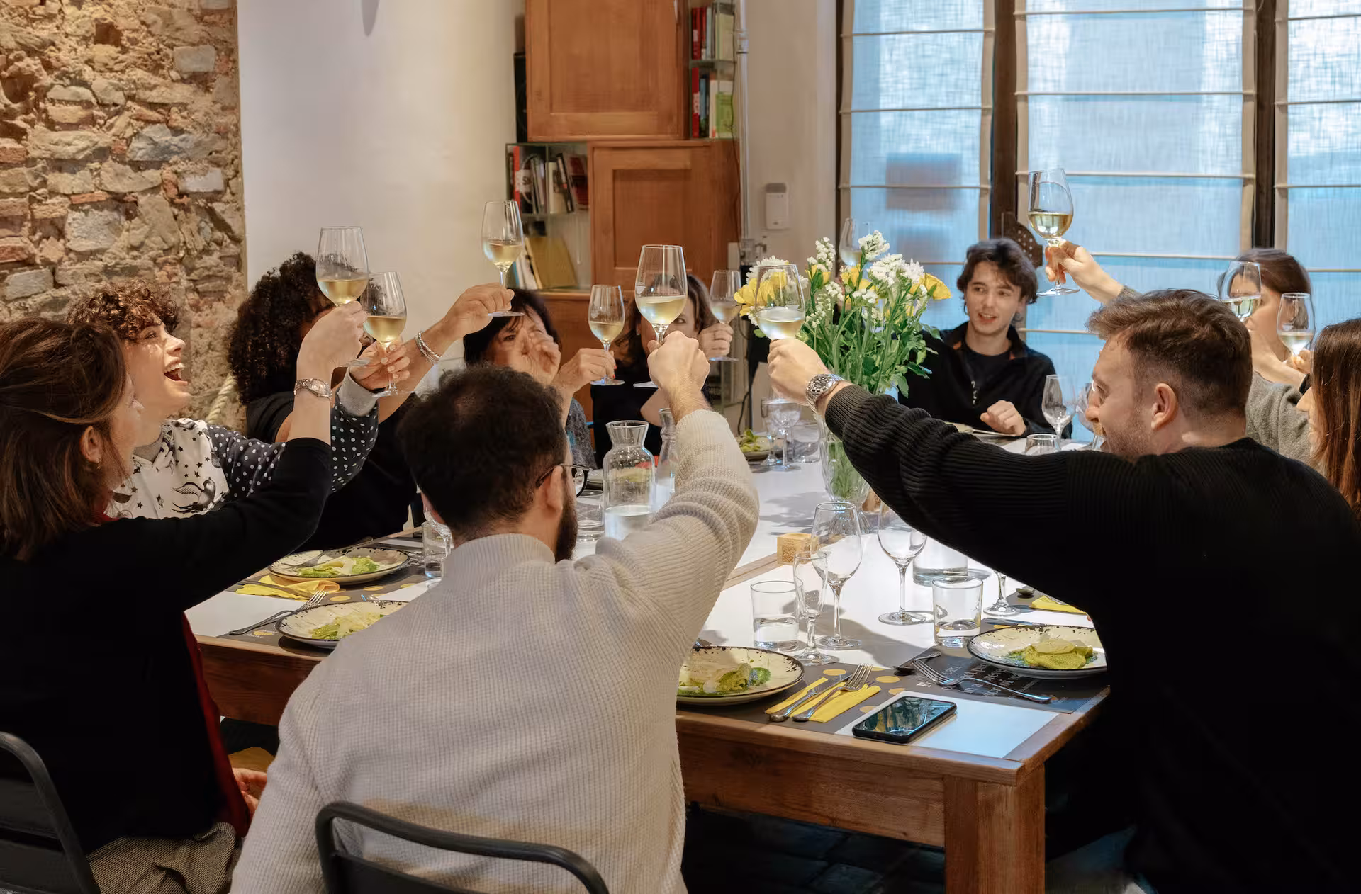 Group of friends enjoying a celebratory toast with wine at a pasta cooking class dinner in Florence.