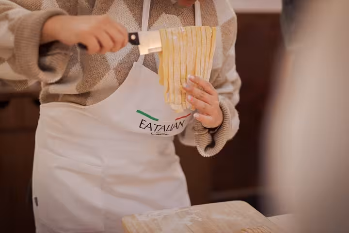 Participant slicing fresh fettuccine during a pasta cooking class in Rome's vibrant Piazza Navona.
