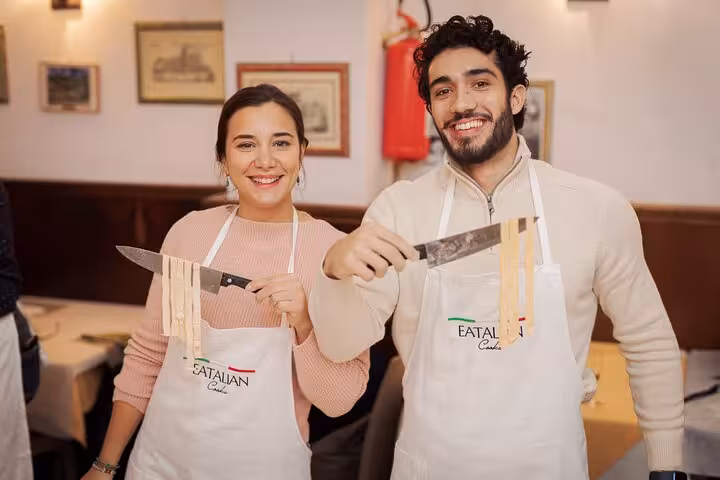 Two happy participants showcasing homemade fettuccine at a pasta cooking class in Rome.