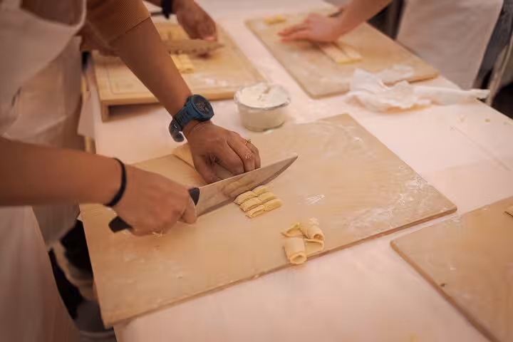 Instructor guides students in making fettuccine pasta at a cooking class in Rome's vibrant Piazza Navona.