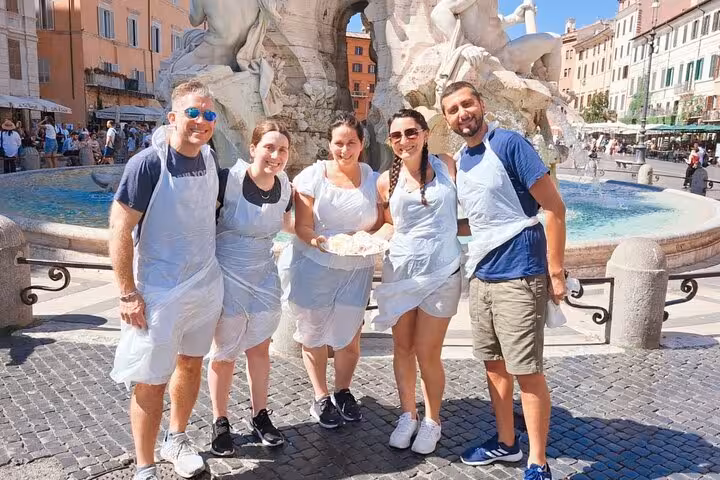 Group of tourists in Rome showcasing fresh pasta near a historic fountain, enjoying a sunny cooking class experience.