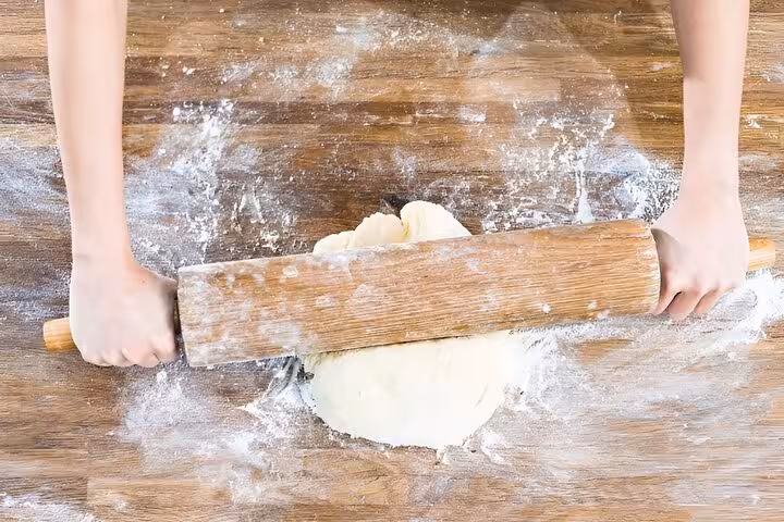 Participant using a rolling pin to flatten dough in a pasta-making class in Florence with a certified chef.