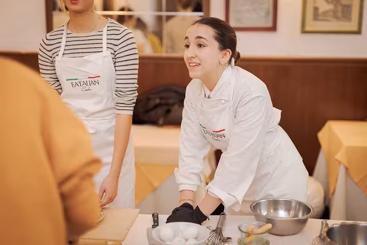 Enthusiastic chef guiding participants in a cooking class at Piazza Navona, Rome, with eggs and utensils on the table.