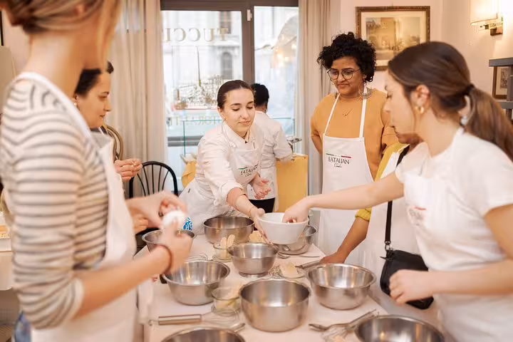 Participants in a pasta and tiramisu cooking class at Piazza Navona, Rome, gather around a table with mixing bowls.