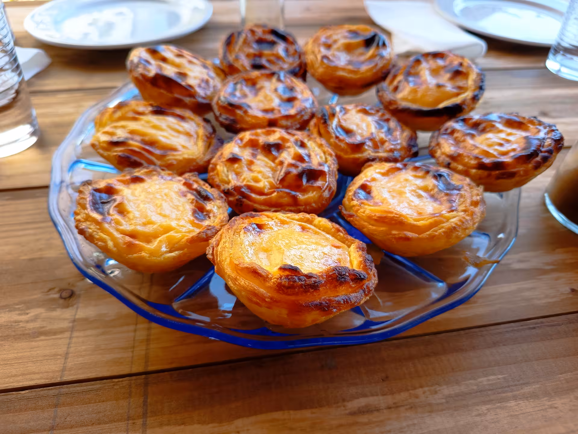 Golden-brown Pastéis de Nata freshly baked and served on a terrace, showcasing Portuguese culinary skills.