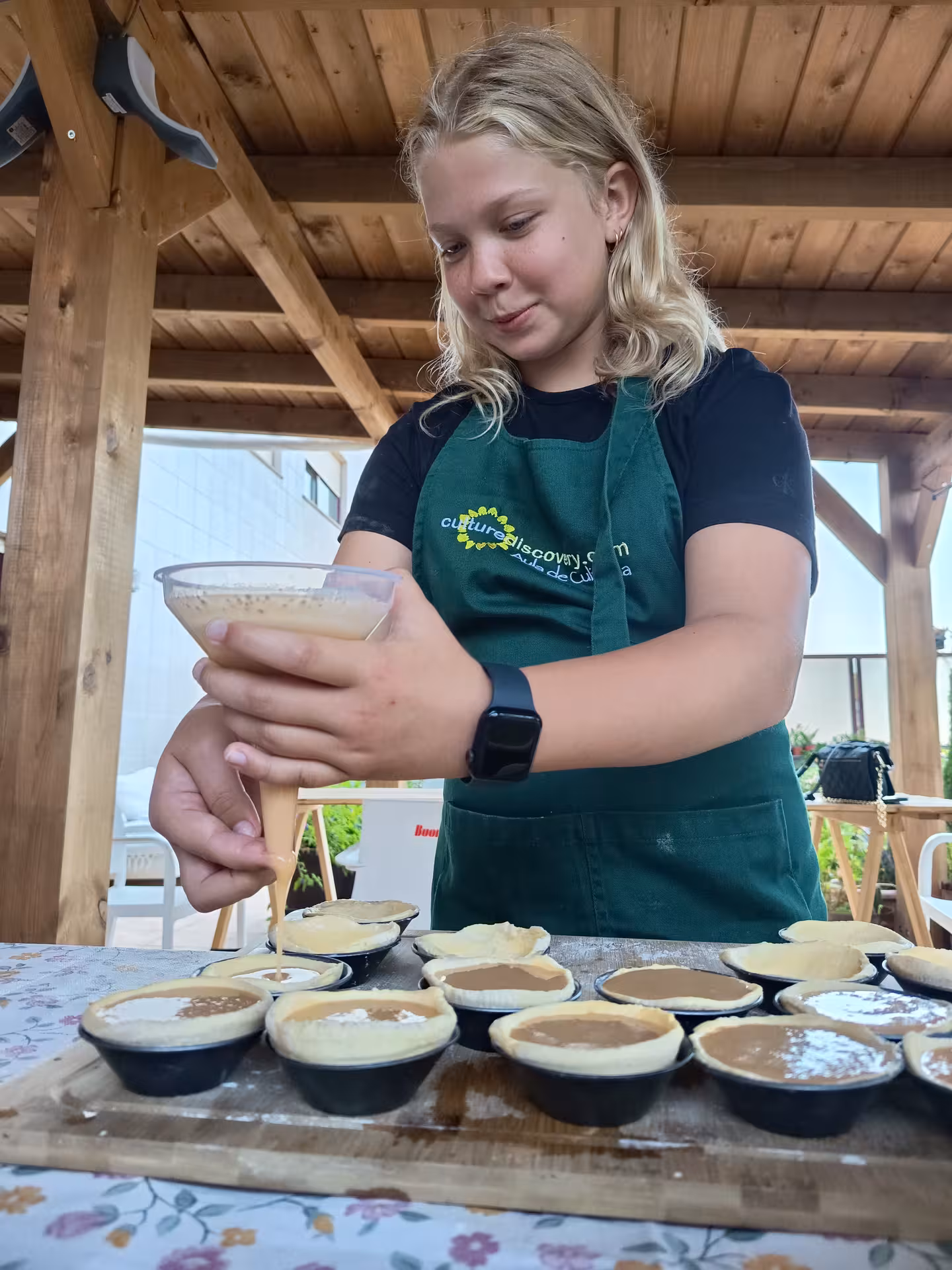 A young participant carefully fills pastry molds with custard during a pastel de nata cooking class.